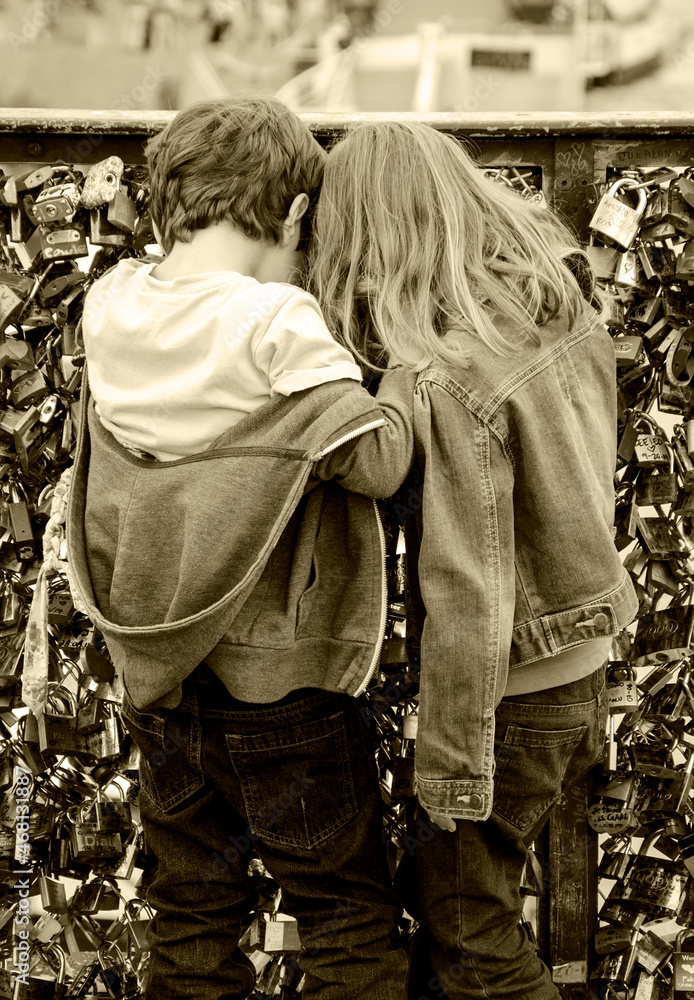 Boy and girl (unrecognizable, back view) playing at Love locks bridge in Paris, France. Valetines day concept. Romantic travel background. Sepia historic photo