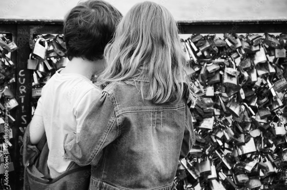 Boy and girl (unrecognizable, back view) playing at Love locks bridge in Paris, France. Valetines day concept. Romantic travel background. Black white historic photo