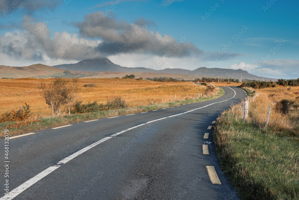 Small S shape asphalt road in a country side. Croagh Patrick mountain on the left in clouds. Travel in Ireland. county Mayo. Stunning Irish landscape. Cloud over peak looks like volcano eruption.
