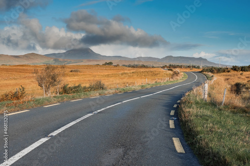 Small S shape asphalt road in a country side. Croagh Patrick mountain on the left in clouds. Travel in Ireland. county Mayo. Stunning Irish landscape. Cloud over peak looks like volcano eruption.