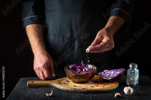 The chef sprinkles the salad with fresh red cabbage salt. Healthy food preparation in the restoran kitchen on a wooden table