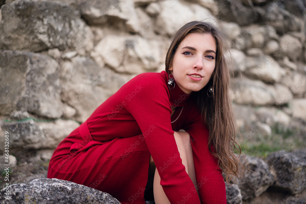 Young girl in the red dress is sitting on stone among the ancient ruins. Young girl in the red dress is sitting on stone among the ancient ruins.