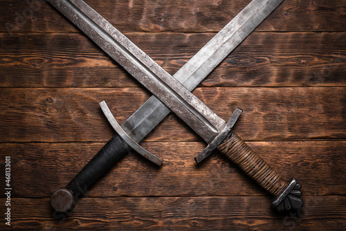 Two crossed swords on the old wooden table flat lay background.