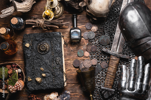 Fotografie Ancient book and knight sword with an armor on the old wooden flat lay table background