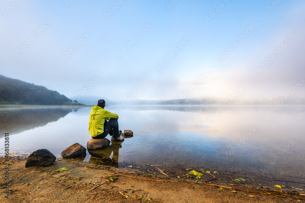 Man sitting besides misty lake