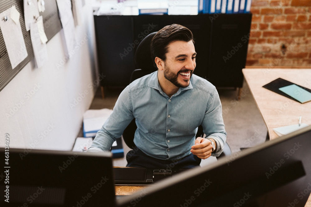 Cheerful business man sitting at desk while looking away Cheerful business man sitting at desk while looking away