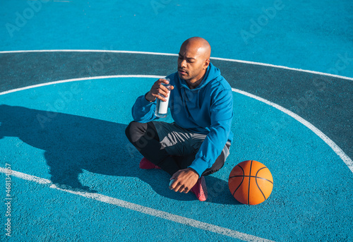 Strong multiracial man resting after training, drinking water from a bottle while sitting © Yakobchuk Olena