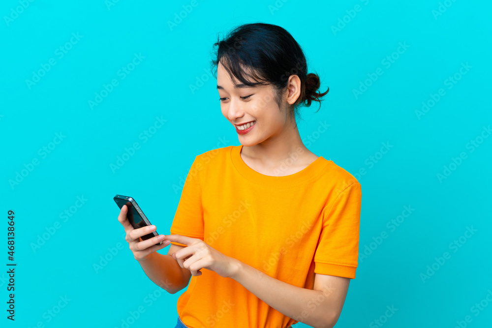 Young Vietnamese woman isolated on blue background sending a message or email with the mobile Young Vietnamese woman isolated on blue background sending a message or email with the mobile