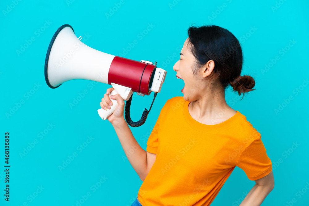 Young Vietnamese woman isolated on blue background shouting through a megaphone to announce something in lateral position Young Vietnamese woman isolated on blue background shouting through a megaphone to announce something in lateral position