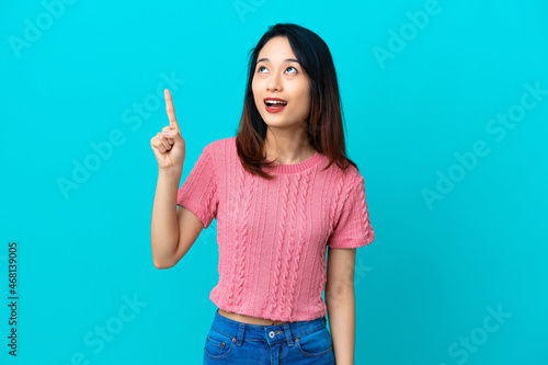 Young Vietnamese woman isolated on blue background pointing up and surprised