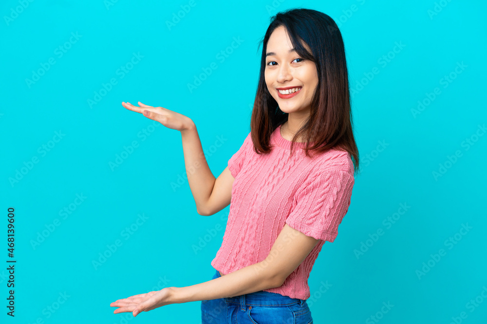Young Vietnamese woman isolated on blue background holding copyspace to insert an ad Young Vietnamese woman isolated on blue background holding copyspace to insert an ad