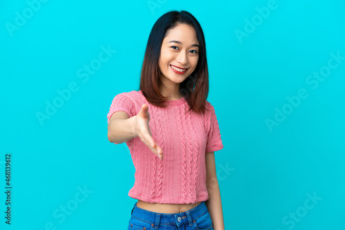 Young Vietnamese woman isolated on blue background shaking hands for closing a good deal