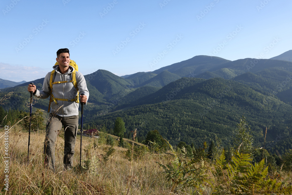 Tourist with backpack and trekking poles hiking through mountains, space for text