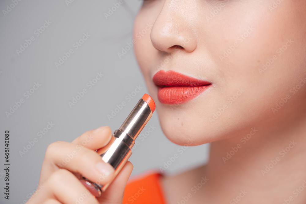 Beautiful young woman putting lipstick on lips