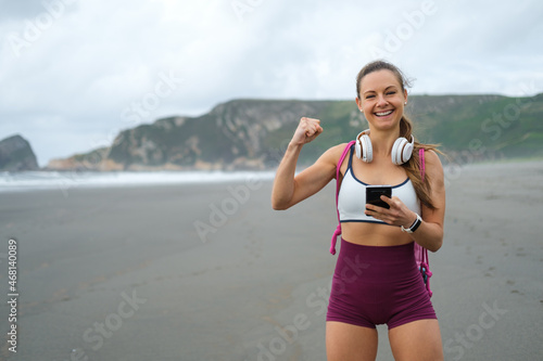 Fitness workout motivation and success. Sporty fit woman celebrating workout achievements on phone app at the beach.