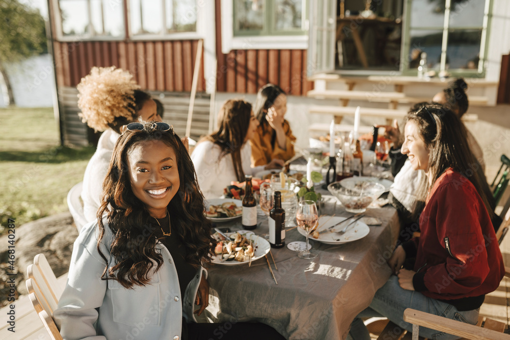 Smiling young woman sitting at dining table with female friends on sunny day Smiling young woman sitting at dining table with female friends on sunny day