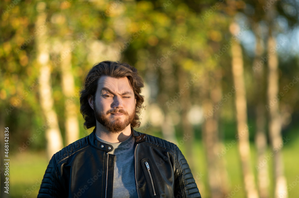 Young bearded man standing and looking at camera against a background of colorful autumn trees Young bearded man standing and looking at camera against a background of colorful autumn trees