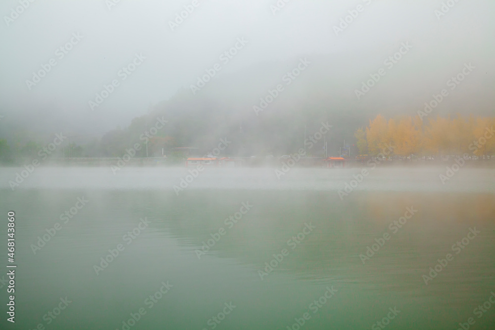 The fog of the early morning reservoir is thick, making the village blurry.