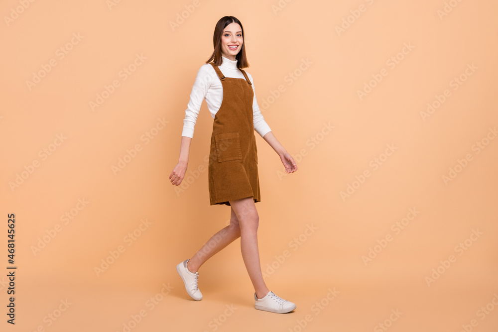 Full size profile photo of adorable satisfied girl walking toothy smile isolated on beige color background Full size profile photo of adorable satisfied girl walking toothy smile isolated on beige color background