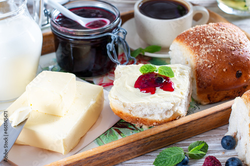 Fresh bread with homemade butter and blackcurrant jam on wooden background.