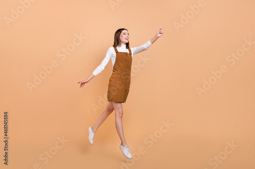 Full body profile portrait of active cheerful girl raise arm look empty space isolated on beige color background