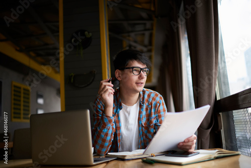 Pensive male student sitting front open laptop computer while looking away. Young man freelancer working remote  with online project on netbook