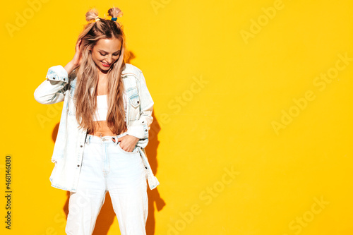 Portrait of young beautiful smiling blond female in trendy summer clothes. Sexy carefree woman posing near yellow wall in studio. Positive model having fun indoors. Cheerful and happy