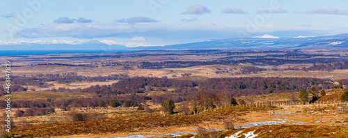 Panorama winter landscape in Patagonia: rolling hills with the Strait of Magellan and snow covered mountains in the background