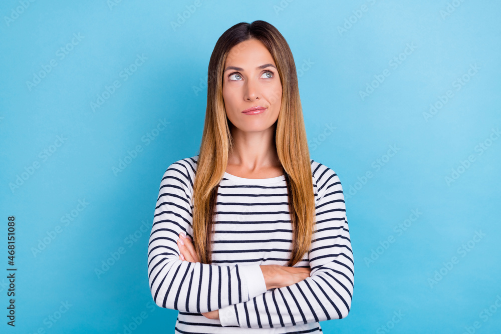 Fototapeta premium Photo of charming unsure young woman dressed striped pullover looking empty space arms crossed isolated blue color background