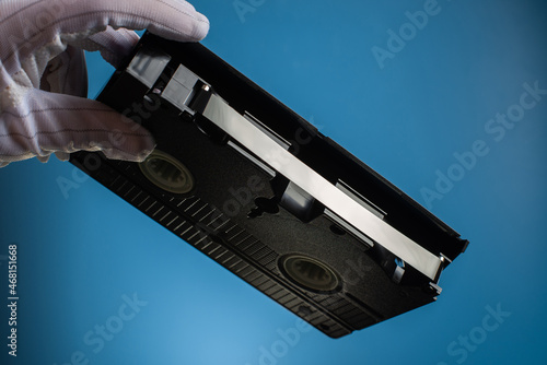 Hand holds retro HVS video cassette on a blue background. Retro wave. 80s 90s. Open film.