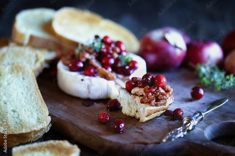 Toasted French bread with baked Camembert Brie cheese and cranberry, honey, balsamic vinegar and nut relish. Selective focus with extreme blurred foreground and background.
