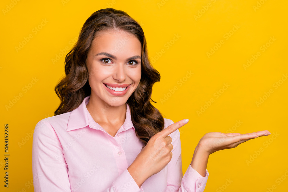 Photo of cute young brunette lady hold indicate empty space wear pink shirt isolated on yellow color background Photo of cute young brunette lady hold indicate empty space wear pink shirt isolated on yellow color background