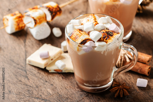 Hot chocolate drink with fried marshmallow in glass cups and winter decoration on wooden table. Concept of cosy Christmas and New Year holidays