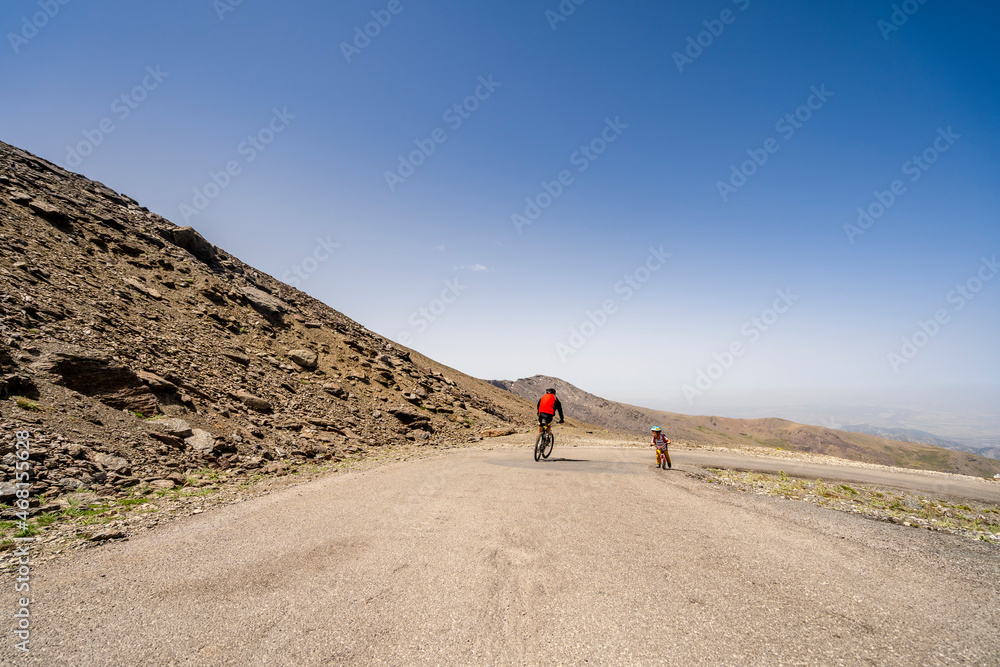 Professional cyclist speeding downhill and small boy biker struggling uphill in Sierra Nevada mountains, Spain Professional cyclist speeding downhill and small boy biker struggling uphill in Sierra Nevada mountains, Spain