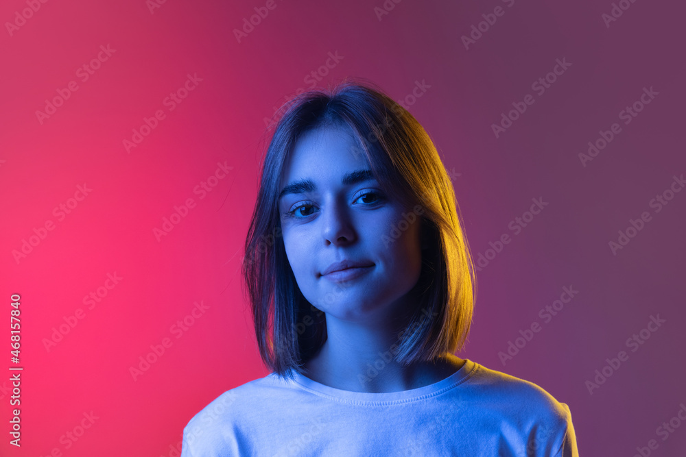 Close-up portrait of young cute girl, student looking at camera isolated on pink-purple studio backgroud in neon. Close-up portrait of young cute girl, student looking at camera isolated on pink-purple studio backgroud in neon.