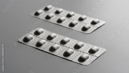 Two gray metallized blisters with medical pills or capsules on a gray background. Duotone. Aspect ratio 16 to 9