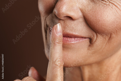 Senior shirtless woman smiling while showing silence gesture