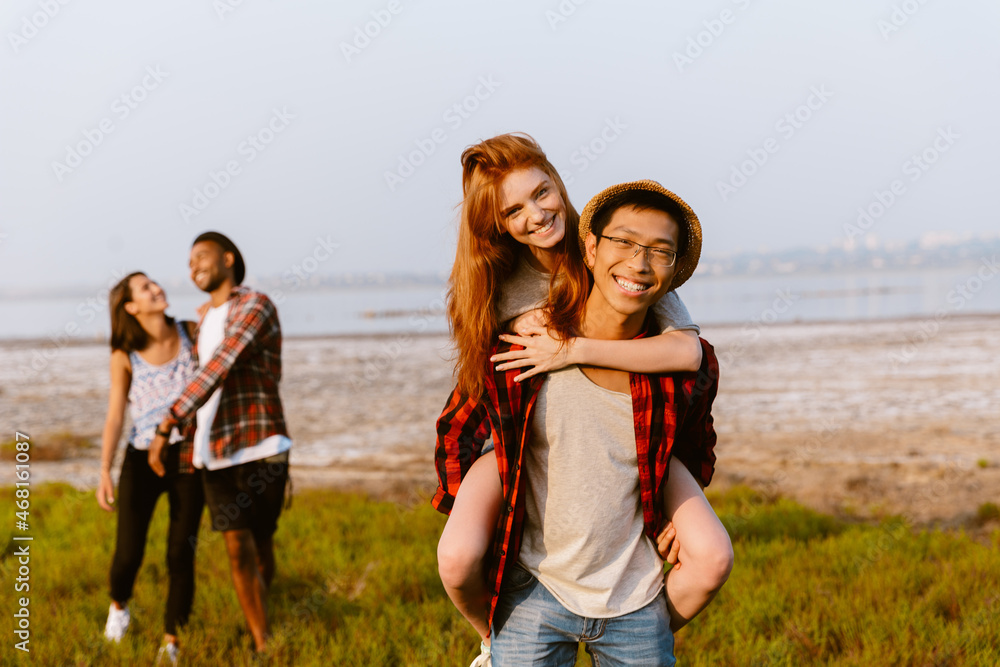 Young multiracial couple piggybacking while resting with his friends Young multiracial couple piggybacking while resting with his friends