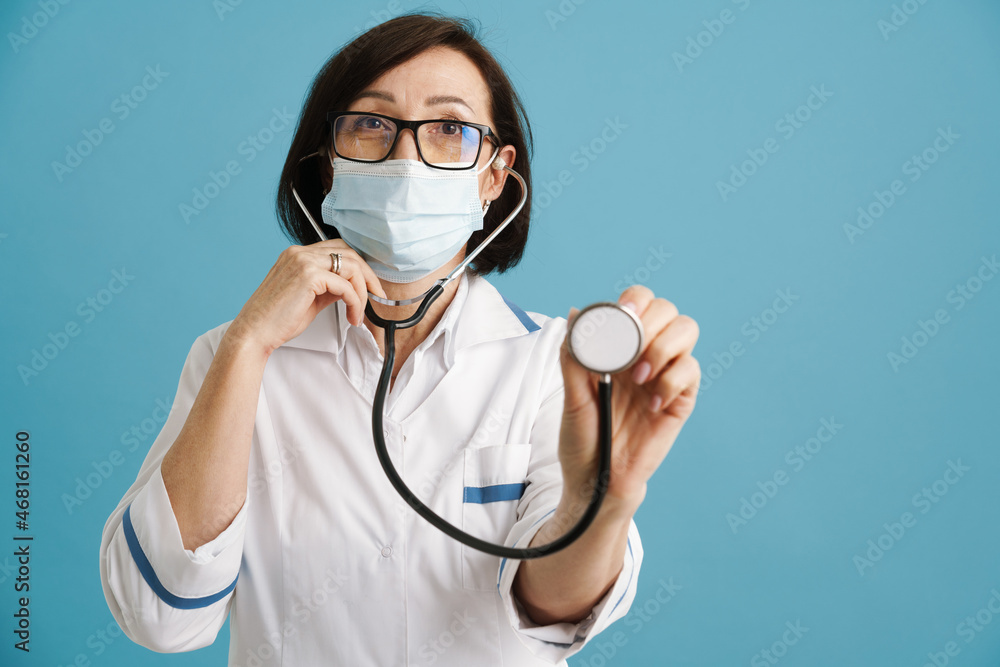 European mature doctor in face mask posing with stethoscope European mature doctor in face mask posing with stethoscope