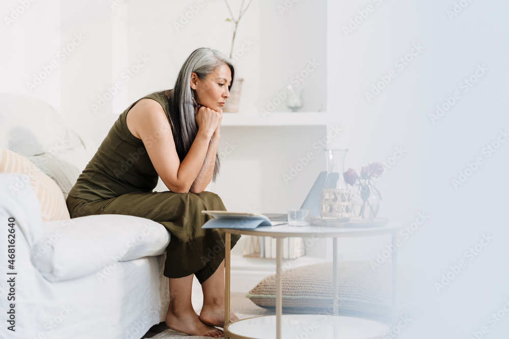 Mature asian woman working with laptop while sitting on couch