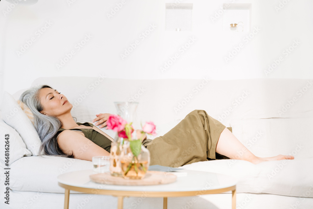 Grey asian woman sleeping with book while lying on couch