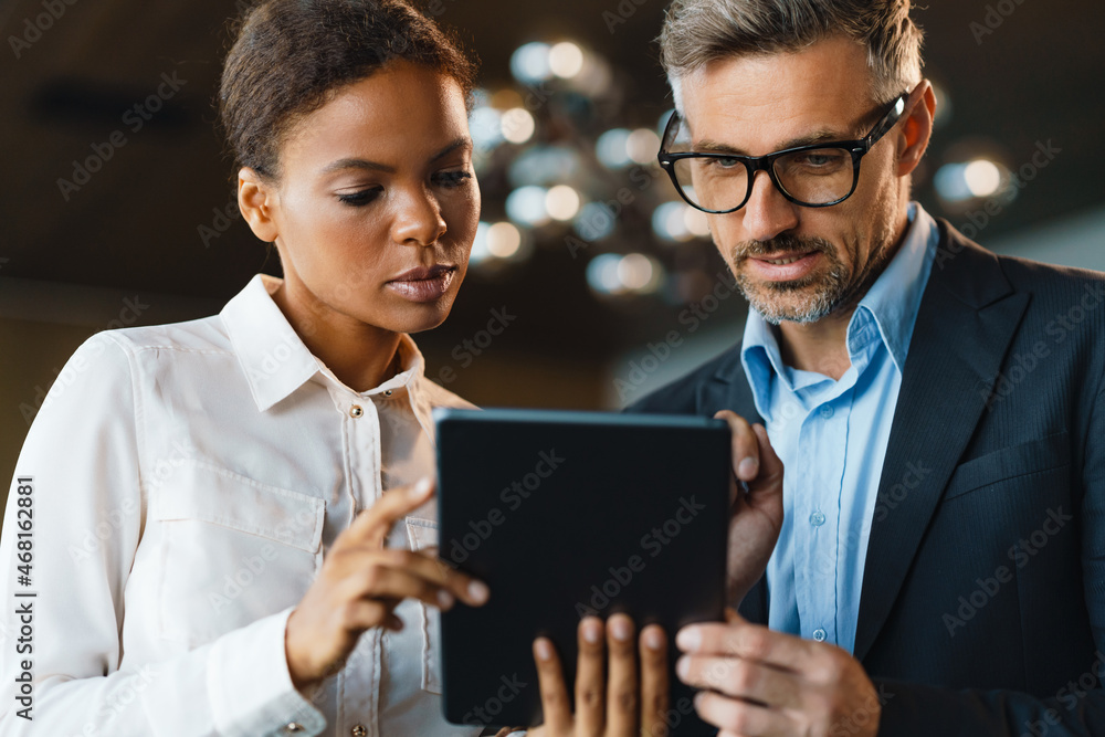 Multiracial woman and man using tablet computer in office - obrazy, fototapety, plakaty 