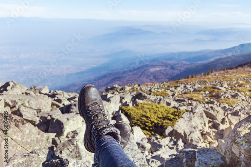 Hiking shoes on a mountain peaks background .Tourist woman sitting on the edge cliff mountains above the city 