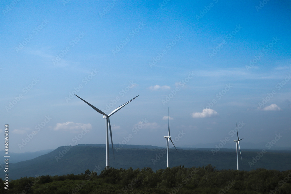 The big white wind turbine for spinning electricity sees large mountains far away, with clouds and blue skies above the mountains. The big white wind turbine for spinning electricity sees large mountains far away, with clouds and blue skies above the mountains.