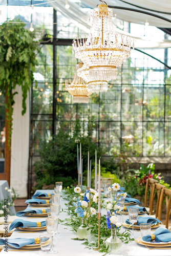 Banquet wedding table setting with blue napkins, gold cutlery, crystal, fresh flowers and candles. Wedding decorations. Soft selective focus.