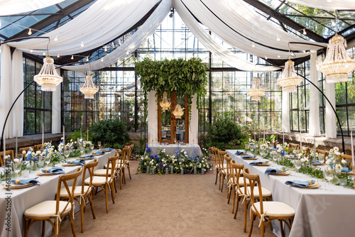 Foto Wedding banquet hall in the greenhouse, tables are set, decorated with fresh flowers, candles, crystal chandeliers