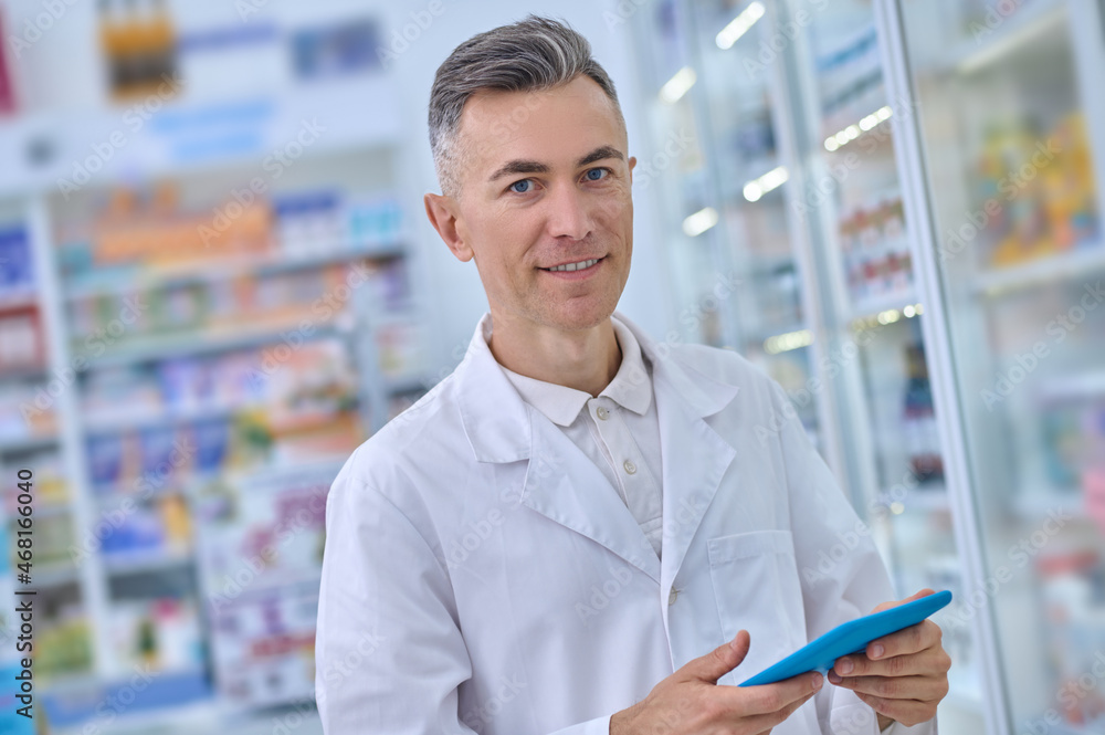 Smiling in medical gown with tablet in pharmacy