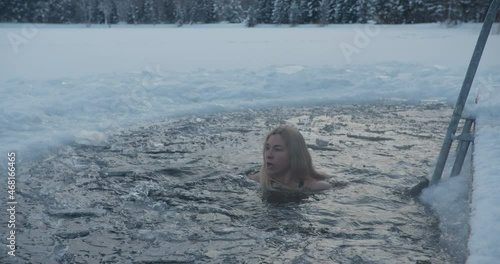 Winter ice hole swimming woman dipping in ice cold water in frozen lake