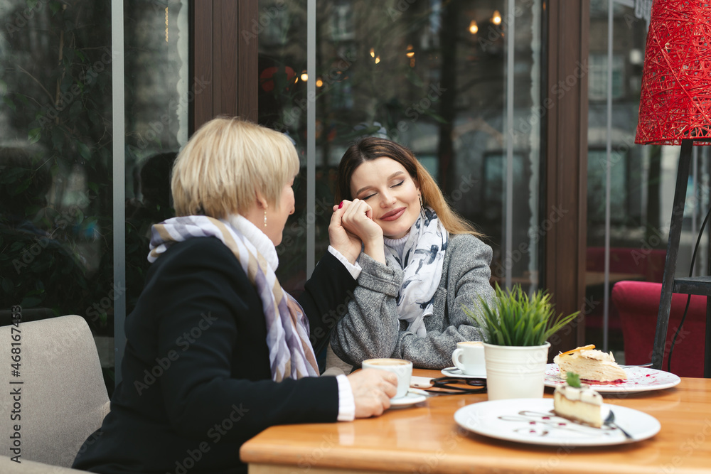 Adult daughter holds her mother's hand and smiles. Emotions of relatives in the cafe Adult daughter holds her mother's hand and smiles. Emotions of relatives in the cafe