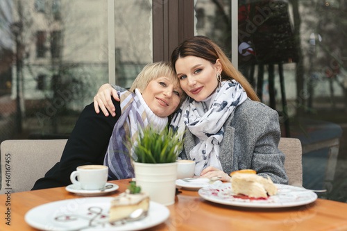 Family day. An elderly woman and her adult daughter drink coffee in a cafe on the sidewalk and hug. Family portrait